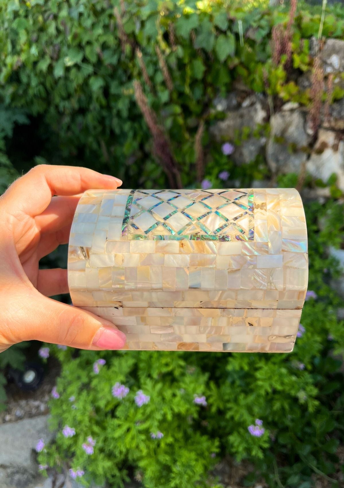 Boîte en bois et nacre, de marqueterie tenue par une main de femme dans un jardin fleuri