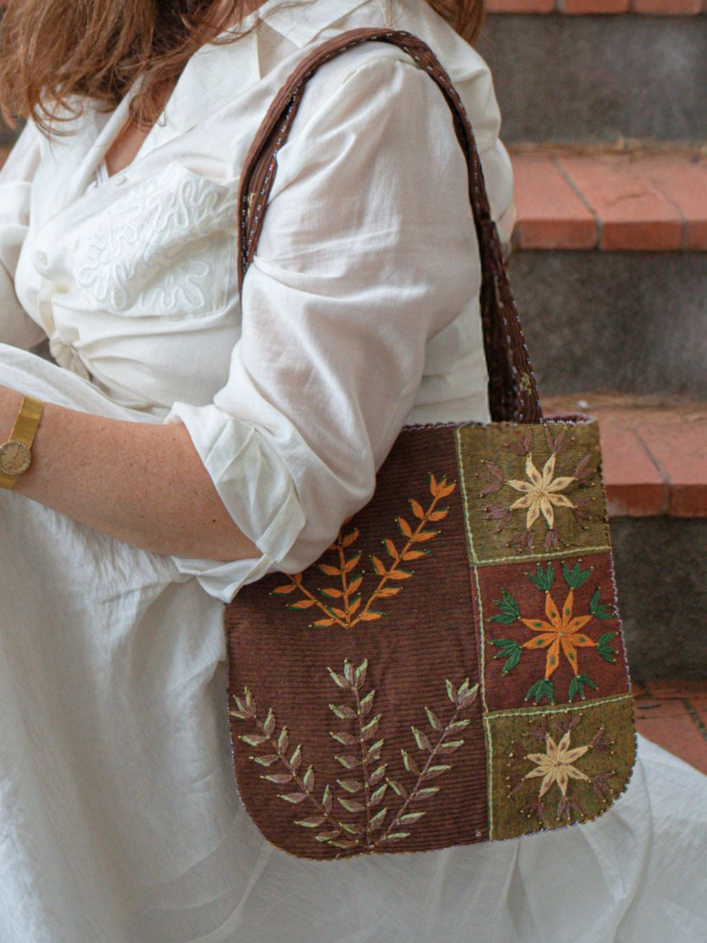 Woman carrying Jardin Velours Nilazur bag, featuring kaki and brown floral embroidery and corduroy details, elegant and comfortable style.