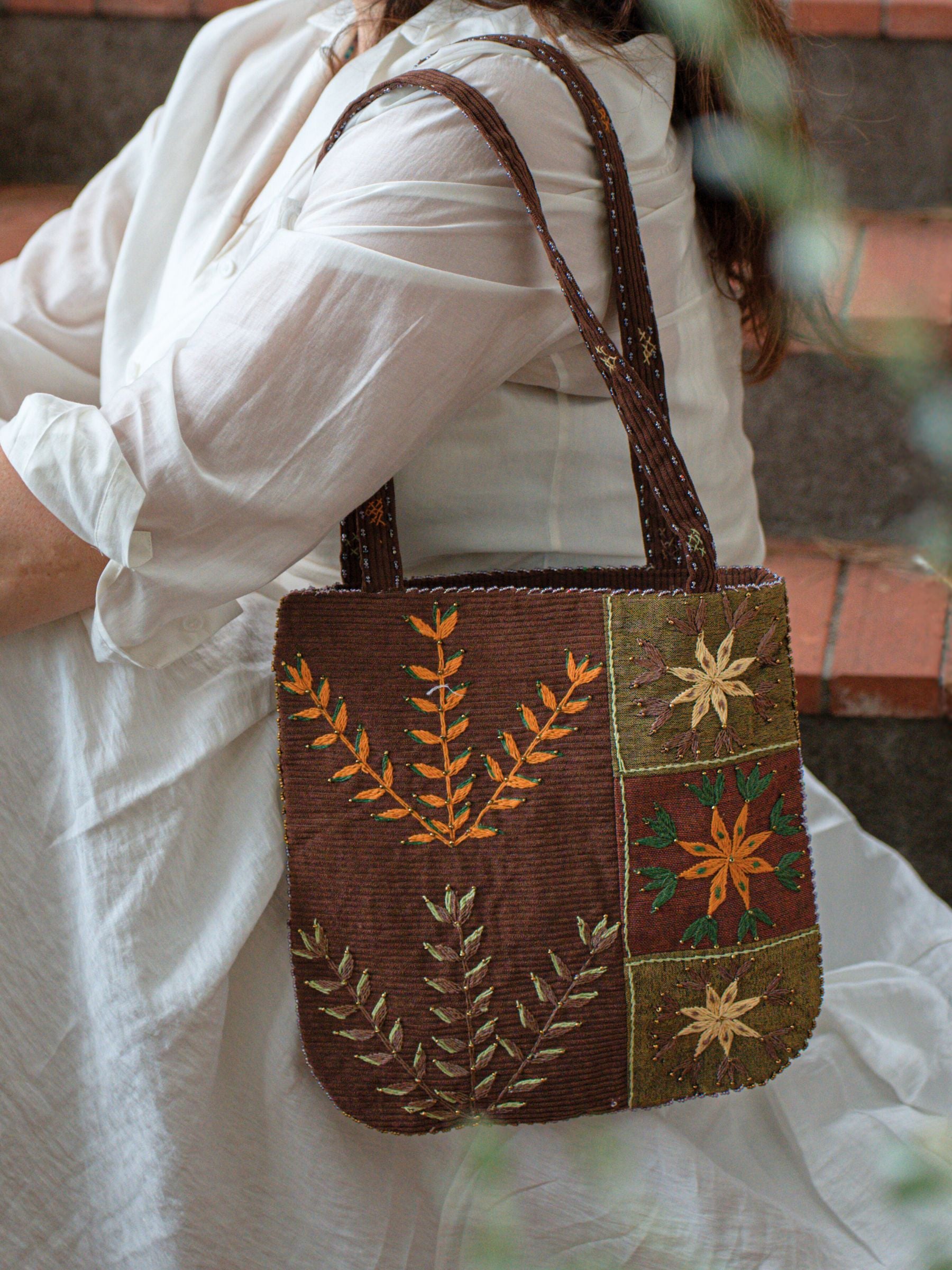Mujer llevando bolso Jardin Velours Nilazur, diseño con bordados florales kaki y marrón, detalles en terciopelo acanalado, estilo elegante y cómodo.