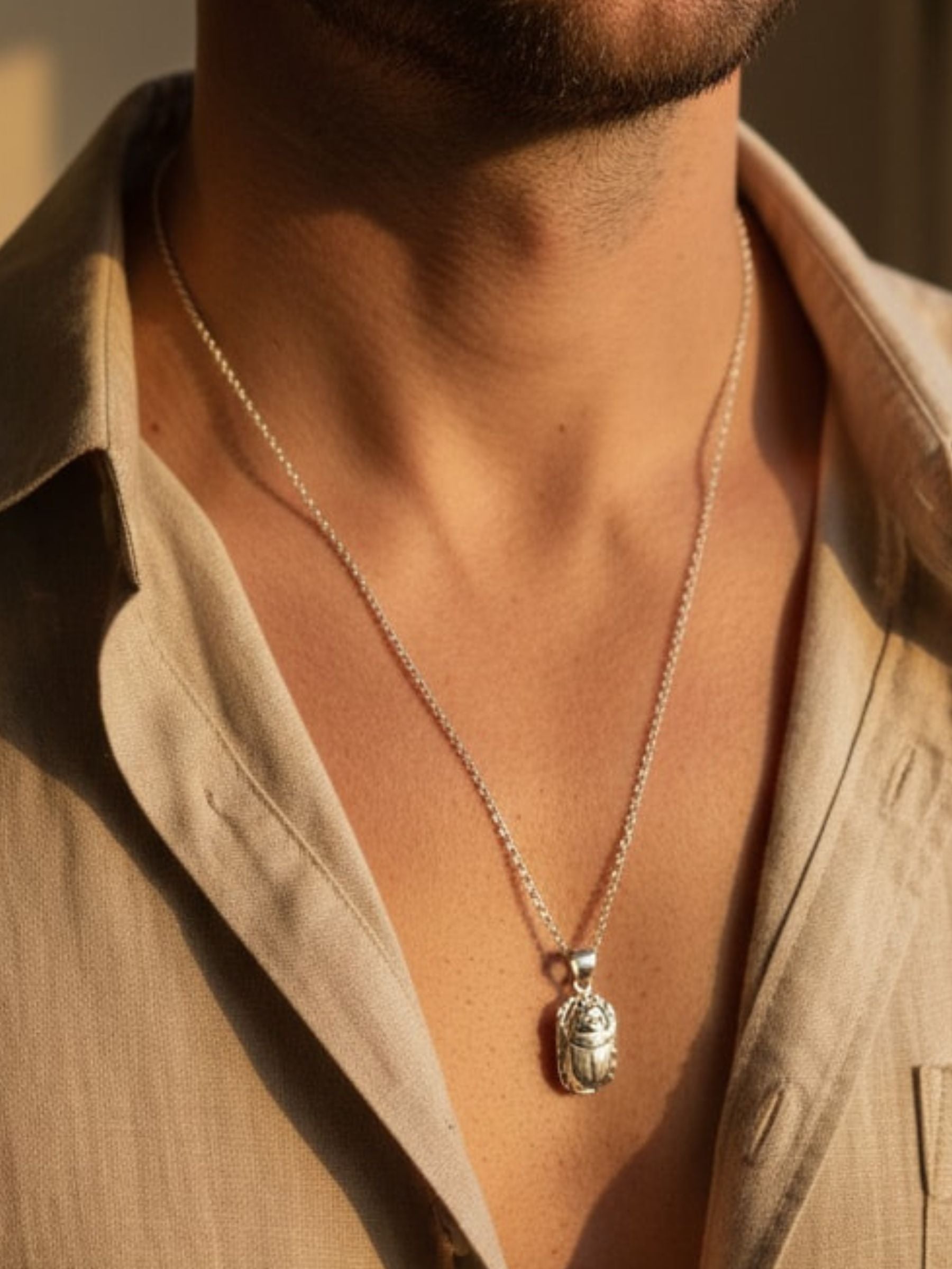 Homme portant un pendentif scarabée égyptien en argent 925 sur une chemise ouverte, symbole de porte-bonheur et de protection